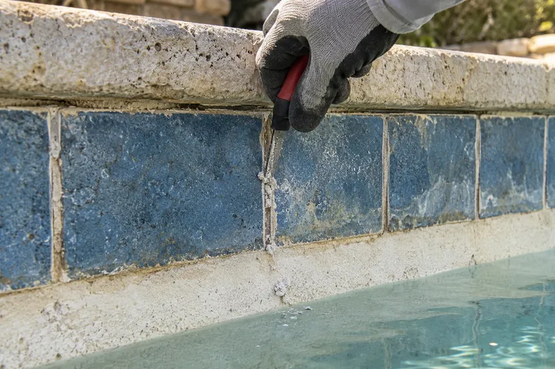 Cracked grout being cleared from waterline tile with a grout saw