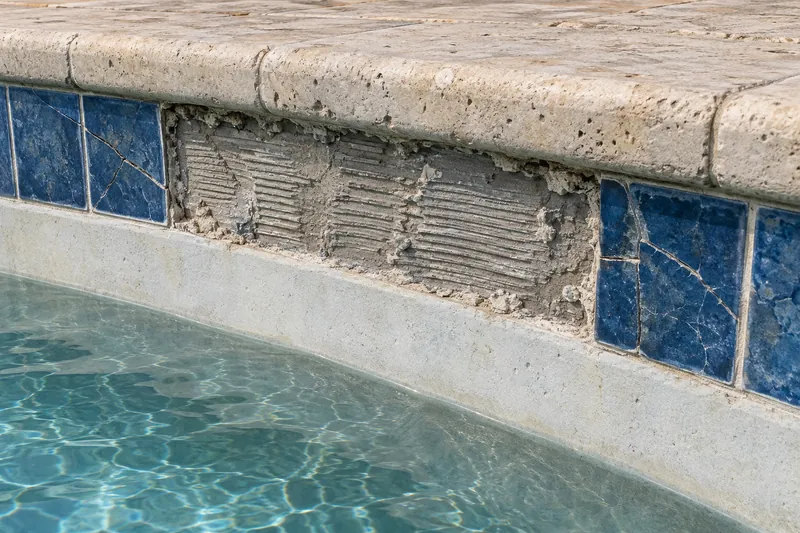 Missing waterline tiles exposing the mortar bed below the pool coping